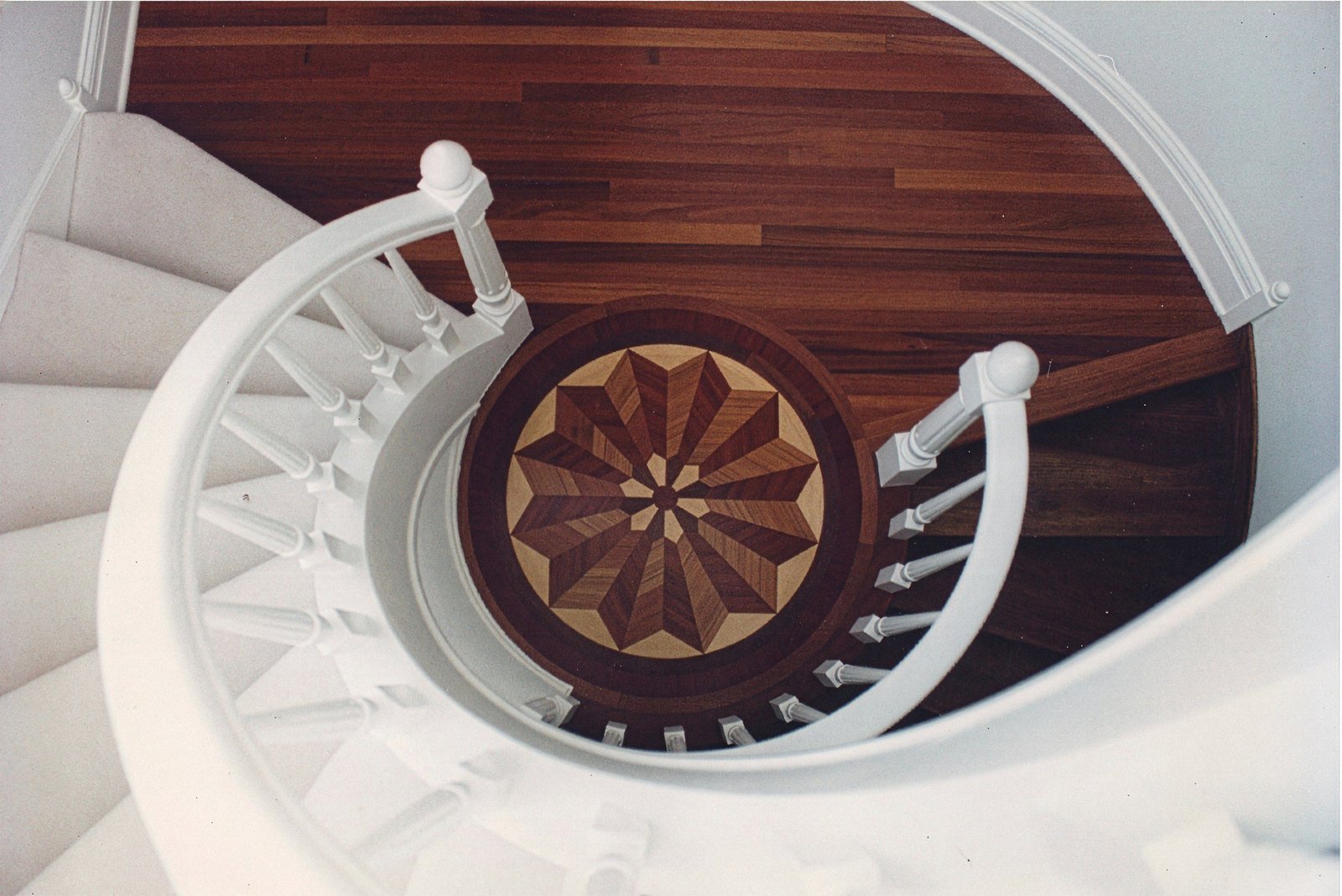 Star medallion set into a plank floor at the foot of a curved staircase, seen from the landing above — custom commission